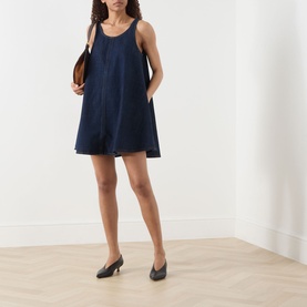 Model wearing FRAME DENIM Duomo dress in navy, relaxed mini silhouette with scoop neck and side pockets, styled with black kitten heels and brown bag