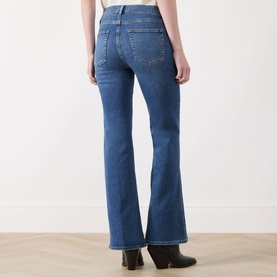 Model wearing FRAME DENIM Flare jeans in Provence blue denim, rear view, styled with black Western ankle boots.