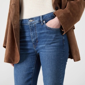 Model wearing FRAME DENIM Flare jeans in Provence blue denim, styled with a brown suede blazer and white knit top.