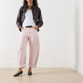 Model wearing FRAME DENIM Taffy pink wide-leg jeans with cuffed hems, styled with dark leather jacket, white tee and black heeled mules.