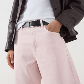Model wearing FRAME DENIM Taffy pink wide-leg jeans, styled with a black leather belt and dark brown leather jacket.
