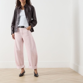 Model wearing FRAME DENIM Taffy jeans in barrel-leg silhouette with turn-up cuffs, styled with dark leather jacket and black flats.
