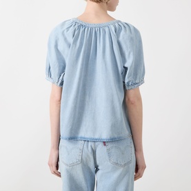 Model wearing FRAME DENIM shirt in Haven blue, back view, showing gathered neckline and puffed short sleeves, styled with light-wash jeans.