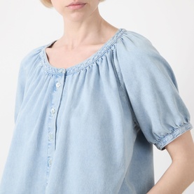 Model wearing FRAME DENIM shirt in Haven blue, featuring gathered scoop neckline, puff sleeves, and button placket in cotton-lyocell blend.