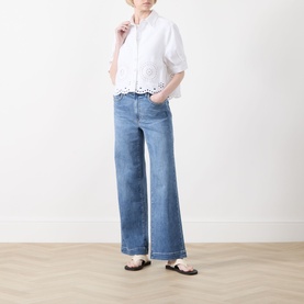 Model wearing FRAME DENIM white broderie anglaise cotton shirt with elbow-length sleeves, styled with wide-leg blue jeans and black flat sandals.