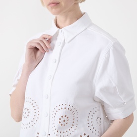Model wearing FRAME DENIM white shirt with broderie anglaise cutwork hem detail and short puffed sleeves, button-front fastening.