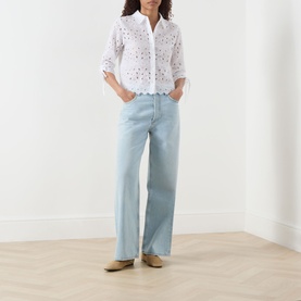 Model wearing FRAME DENIM The Paisley Eyelet Cinch-Sleeve Shirt in white with scalloped hem, styled with pale blue wide-leg jeans and tan loafers
