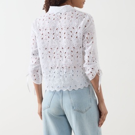 Model wearing FRAME DENIM The Paisley Eyelet Shirt in white, showing back view with scalloped hem and cinched sleeves, styled with light blue jeans.