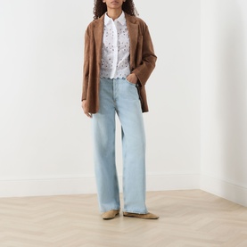 Model wearing FRAME DENIM The Paisley Eyelet Shirt in white with scalloped hem, styled with brown blazer and light-wash wide-leg jeans.