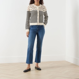 Model wearing FRAME DENIM Daylily Raw Fray straight jeans in mid-blue with raw fray hem, styled with a cream striped crochet cardigan and black flats.