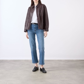 Model wearing FRAME DENIM Gossamer straight jeans in light blue, styled with a dark brown leather jacket and black loafers.