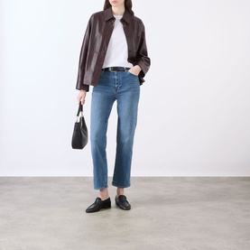 Model wearing FRAME DENIM Gossamer straight jeans in mid-blue, styled with a dark brown leather jacket, white tee and black loafers