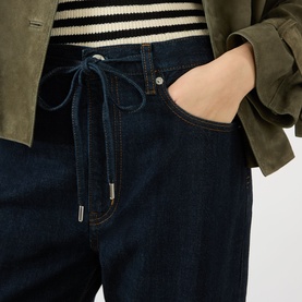 Model wearing FRAME DENIM The Off Duty Drawstring Bow High-Rise Barrel Jeans in Rinse, styled with a striped top and olive suede jacket.