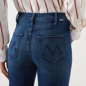 Model wearing Mother Jeans in Homecoming High mid-blue denim, rear view showing M-stitched back pockets and slim fit, styled with striped shirt.