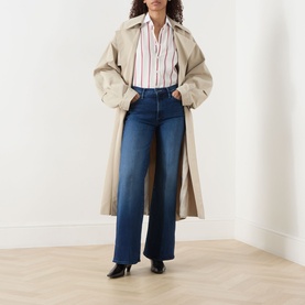 Model wearing Mother Homecoming High jeans in dark blue wide-leg style, styled with a striped shirt and beige trench coat