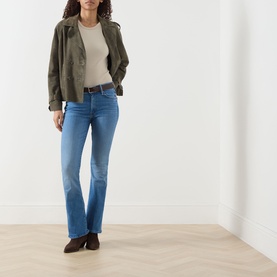Model wearing Mother Jeans in Piece By Piece, mid-blue bootcut denim, styled with khaki jacket, cream top and brown ankle boots.