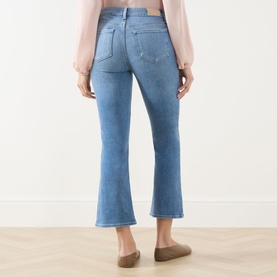 Model wearing Paige Crop Boot jeans in Cinerama blue denim, rear view, styled with a blush top and tan flats.