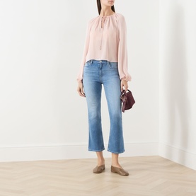 Model wearing Paige Crop Boot jeans in Cinerama, a mid-blue wash with flared hem, styled with a blush top and taupe flats.