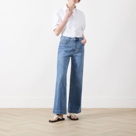 Model wearing Paige Straight Jeans in Encino mid-blue denim with wide leg and cuffed hem, styled with white shirt and brown sandals.
