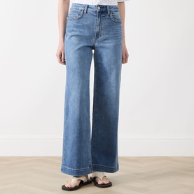 Model wearing Paige straight jeans in Encino blue denim, wide-leg cut with contrast stitching, styled with black sandals