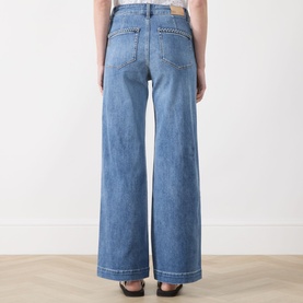 Model wearing Paige straight jeans in Encino blue denim, rear view showing wide leg, contrast stitching and patch pocket detail.