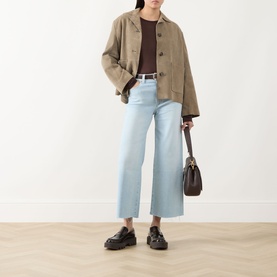 Model wearing Paige Motif straight-leg jeans in light blue denim, styled with a khaki jacket, brown top, and black loafers