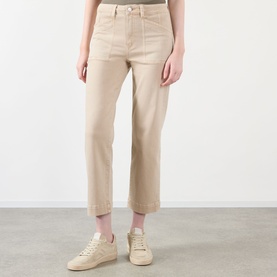 Model wearing Paige straight jeans in Vintage Warm Sand with turn-up hems, styled with white trainers.