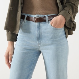 Model wearing Paige Coliseum straight jeans in light blue denim, styled with a dark brown belt and olive green jacket.