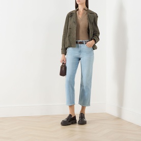 Model wearing Paige Coliseum straight-leg jeans in light blue denim, styled with an olive jacket, tan top, and black loafers.