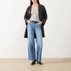 Model wearing Paige Straight Jeans in Cinerama light blue denim, styled with a dark brown leather coat and grey vest top.