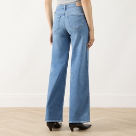 Model wearing Paige Straight Jeans in Cinerama blue, wide-leg silhouette, rear view, styled with black heeled boots.