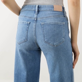 Model wearing Paige straight-leg jeans in Cinerama blue denim, rear view showing back pockets and wide-leg silhouette.