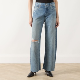 Model wearing Paige Wide Leg Jeans in Terazzo Deconstructed, light blue denim with ripped knee and raw hem, styled with black ankle boots