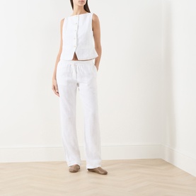 Model wearing Samsoe & Samsoe white linen sleeveless blouse with button front, styled with matching white linen trousers.
