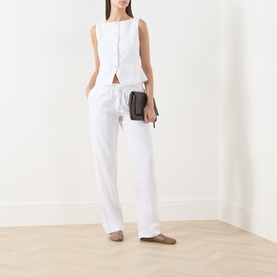 Model wearing Samsoe & Samsoe white linen sleeveless blouse with matching wide-leg trousers, carrying a small dark crossbody bag.