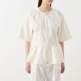 Model wearing Samsoe & Samsoe Satoman Peplum Blouse in Egret, featuring zip front, short sleeves and peplum hem, styled with white trousers.