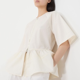 Model wearing Samsoe & Samsoe Satoman Peplum Blouse in Egret, featuring short flared sleeves, zip fastening and peplum hemline.