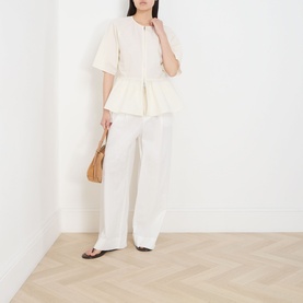 Model wearing Samsoe & Samsoe Satoman Peplum Blouse in Egret with wide-leg white trousers, carrying a tan woven bag.