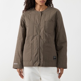Model wearing Samsoe & Samsoe Major Brown quilted collarless jacket with patch pockets, styled with white trousers.