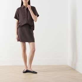 Model wearing Samsoe & Samsoe Saagnet Mini Skirt in Mulch, styled with matching short-sleeve shirt and black ballet flats.