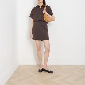 Model wearing Samsoe & Samsoe Saagnet Mini Skirt in Mulch, styled with a matching polo top, tan shoulder bag and black ballet flats.