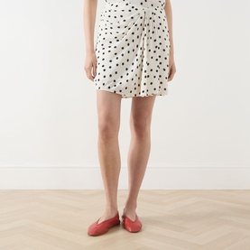 Model wearing Samsoe & Samsoe Saiben Polka Dot Skirt in Drifting Dots Egret, mini length with asymmetric hem, styled with red flat shoes