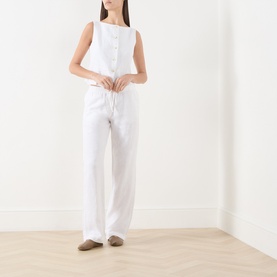Model wearing Samsoe & Samsoe white linen trousers with drawstring waist, styled with a white sleeveless top and taupe flat shoes.