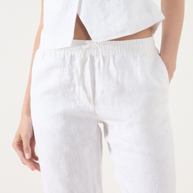 Model wearing Samsoe & Samsoe white linen trousers with elasticated drawstring waistband and side pocket, styled with a white crop top.