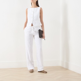 Model wearing Samsoe & Samsoe white linen trousers with drawstring waist, styled with a matching white sleeveless top and carrying a dark clutch bag.
