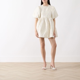 Model wearing Sister Jane Chalk Mini Dress in white jacquard with puff sleeves and voluminous flared skirt, styled with cream heeled mules