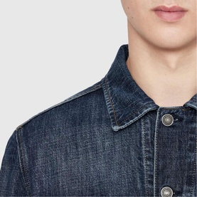 Model wearing All Saints dark indigo denim jacket, close-up showing spread collar and silver-tone buttons