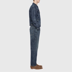 Model wearing All Saints dark indigo denim jacket and jeans in a relaxed fit, styled with tan suede boots, side profile view.
