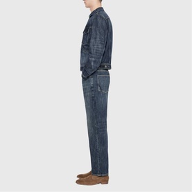 Model wearing All Saints dark indigo denim jacket and matching jeans, styled with tan leather shoes, side profile view.