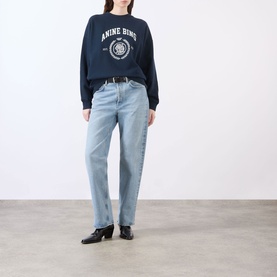 Model wearing Anine Bing Miles Collegiate Logo Sweatshirt in navy with light-wash straight-leg jeans and black heeled boots.